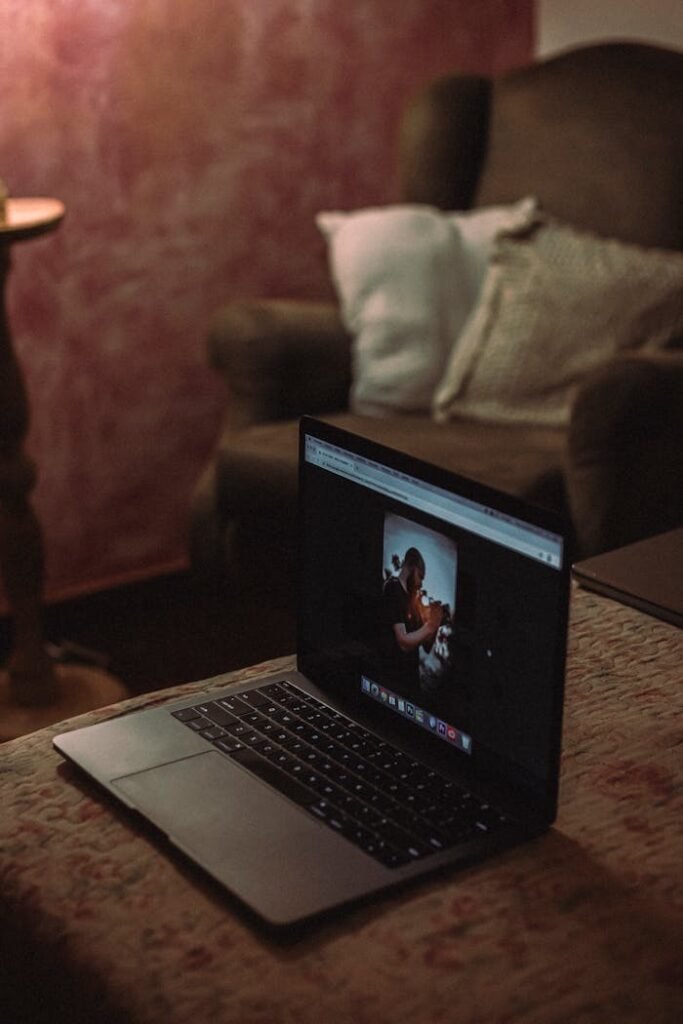 A laptop displaying a photo is set on a table in a dimly lit cozy living room.