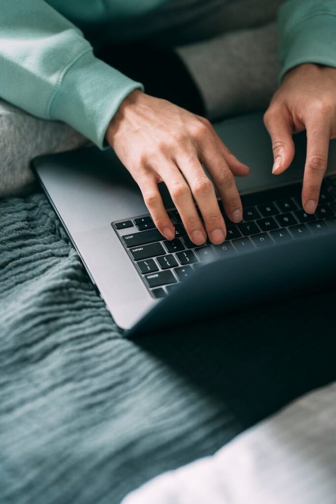 Close-up of hands typing on a laptop keyboard on a cozy home desk setting.